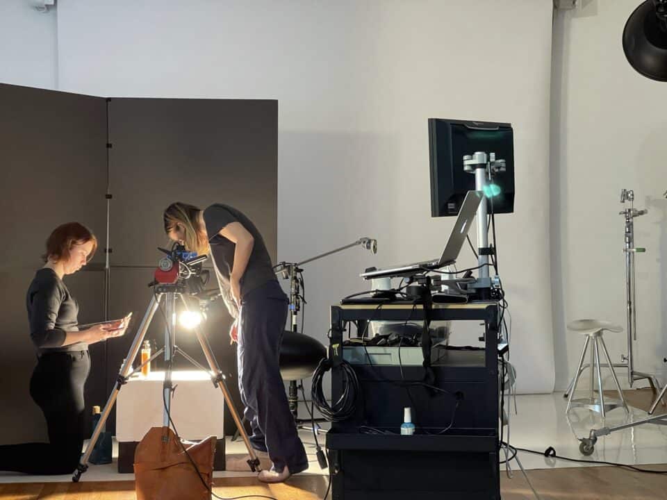 Professional photography workspace with camera, contact sheets, retouched image prints, lighting notes, and visual campaign references.