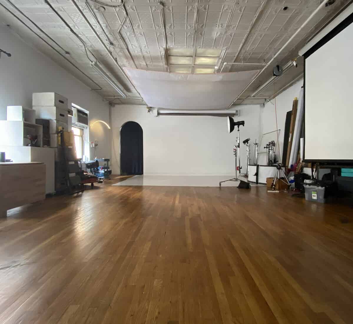 Spacious NYC photo studio rental with large windows, professional lighting equipment, seamless backdrop, makeup area, and open shooting space.