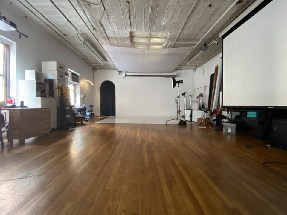 Spacious NYC photo studio rental with large windows, professional lighting equipment, seamless backdrop, makeup area, and open shooting space.
